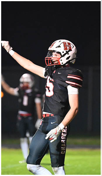 A person wearing a football uniform and helmet is raising one arm in celebration on a field at night with another similarly dressed person blurred in the background. Description generated by AI