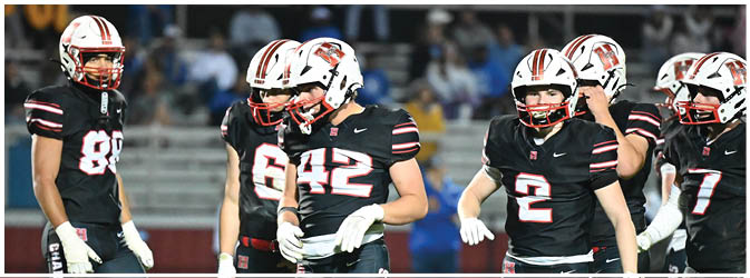 Four people wearing black football uniforms with white gloves stand on a field, appearing to prepare for a play. Description generated by AI