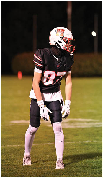 A person wearing a black football uniform and white helmet with red faceguard is standing on a grassy field at night. Description generated by AI