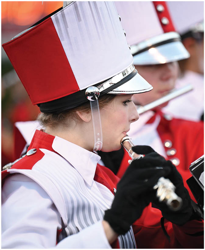 People in marching band uniforms are playing flutes while reading sheet music attached to their instruments. Description generated by AI