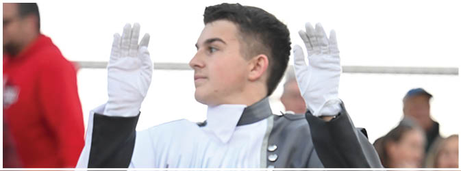 A person with dark hair is peeking over a white surface with both hands raised and wearing white gloves. Description generated by AI
