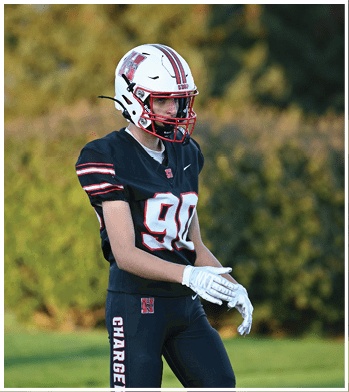 A person wearing a black football uniform with the number 90 and white gloves is standing outdoors on a grassy field with trees in the background. Description generated by AI