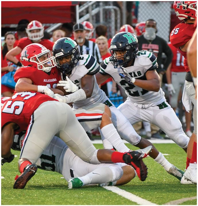 Three football players in blue and white uniforms running on a field. Description generated by AI