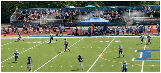 Three football players in blue and white uniforms running on a field. Description generated by AI