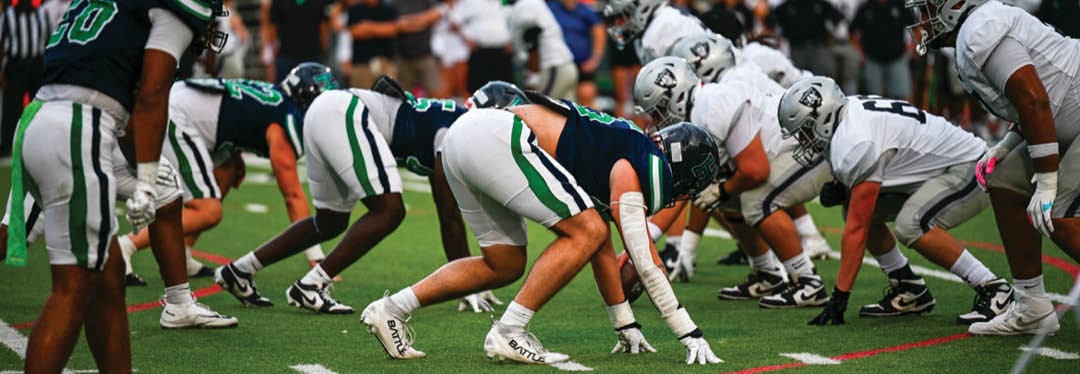 Four people wearing black sports jerseys with “VISTA" on them stand closely together in front of a large crowd, with one person raising an arm in celebration. Description generated by AI