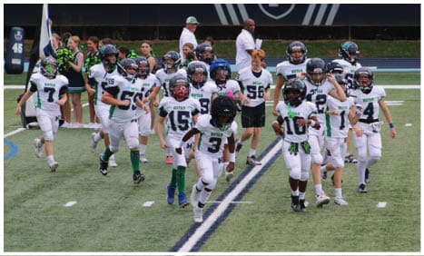Three football players in blue and white uniforms running on a field. Description generated by AI