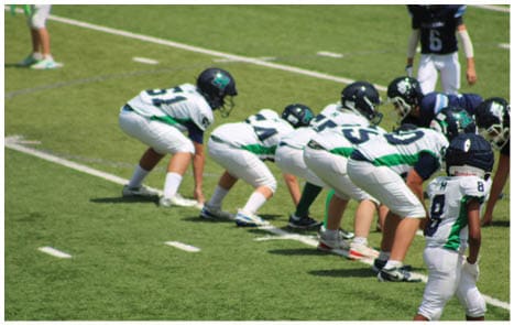 Three football players in blue and white uniforms running on a field. Description generated by AI