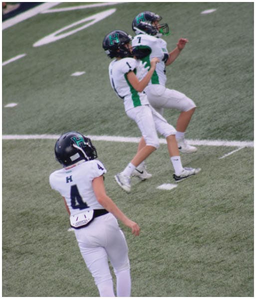 Three football players in blue and white uniforms running on a field. Description generated by AI