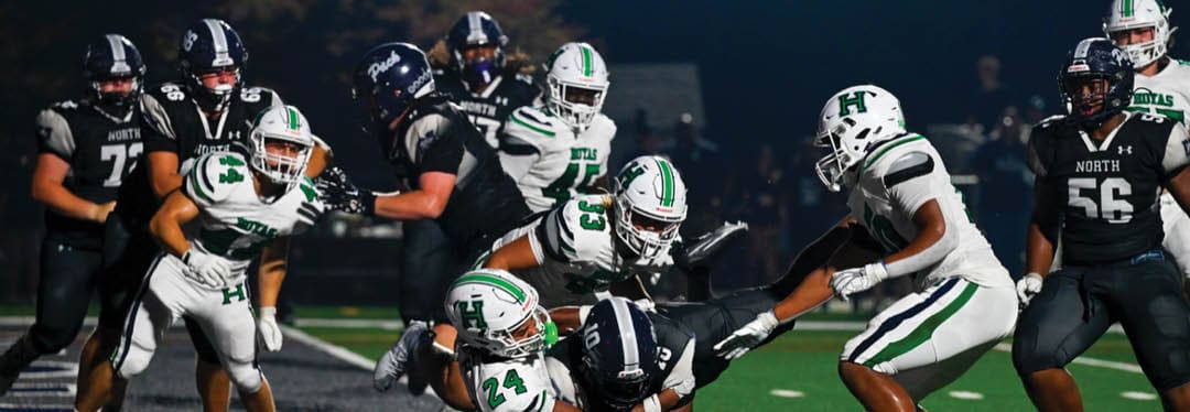Four people wearing black sports jerseys with “VISTA" on them stand closely together in front of a large crowd, with one person raising an arm in celebration. Description generated by AI