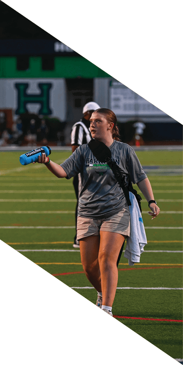 Two football players are on the field, one jumping in the air while the other is running. A referee is also present, watching the play. AI generated content