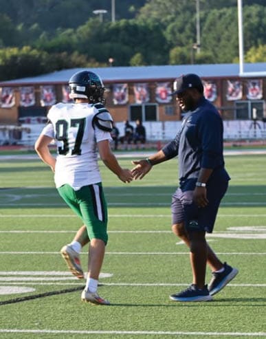 Two men embrace on a field, one wearing a black shirt and the other wearing a black and white shirt. AI generated content