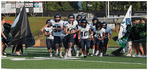 Three football players in blue and white uniforms running on a field. Description generated by AI