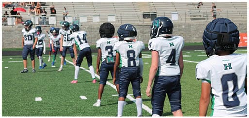 Three football players in blue and white uniforms running on a field. Description generated by AI