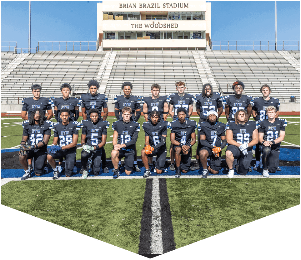 A group of people wearing matching dark sports uniforms pose for a team photo on a football field with empty stadium bleachers and a building labeled Brian Brazil Stadium in the background. Description generated by AI