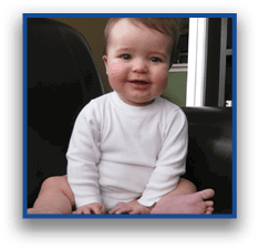 A child wearing a white long-sleeve shirt is sitting on a dark leather surface with legs spread and hands resting in front. Description generated by AI