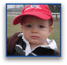 A child wearing a red cap and a dark jacket with a white collar is standing outdoors in front of a chain-link fence. Description generated by AI