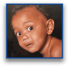 A child with short curly hair looks over their shoulder with wide eyes against a dark background. Description generated by AI