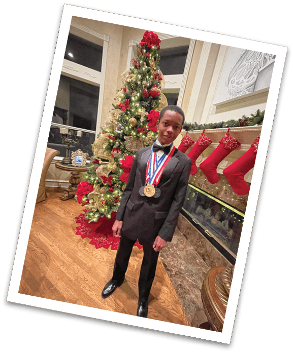 A person dressed in a black suit with a bow tie stands indoors near a decorated Christmas tree and fireplace wearing multiple medals around their neck. Description generated by AI