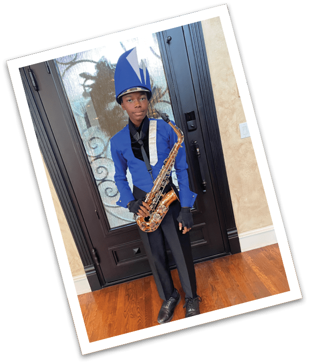 A person dressed in a blue and black marching band uniform with a tall blue hat is holding a saxophone while standing indoors in front of a glass door. Description generated by AI