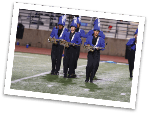 People in blue and black marching band uniforms with tall blue hats are playing saxophones while marching on a field. Description generated by AI