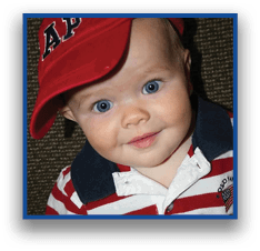 A child with blue eyes wearing a red and white striped polo shirt and a red hat is smiling while looking at the camera. Description generated by AI