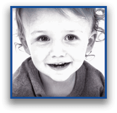 A smiling child with curly hair is wearing a dark shirt and looking directly at the camera. Description generated by AI