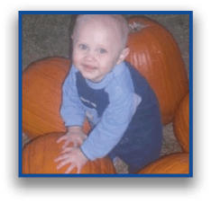A child wearing a blue outfit is sitting among several large pumpkins on a bed of straw. Description generated by AI