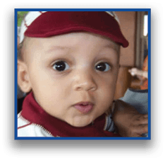 A child wearing a white and maroon striped shirt looks toward the camera while being held by an adult. Description generated by AI
