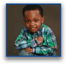 A child wearing a green and blue plaid shirt is sitting with arms crossed and smiling against a plain dark background. Description generated by AI