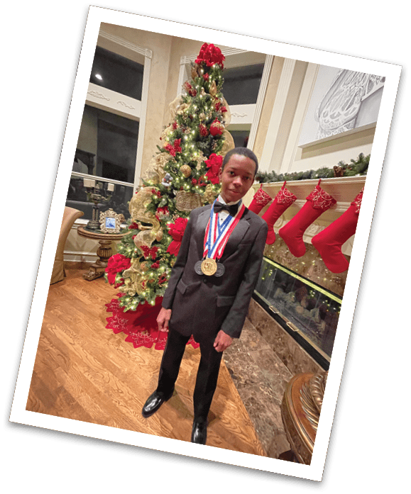A person dressed in a black suit with a bow tie stands indoors near a decorated Christmas tree and fireplace wearing multiple medals around their neck. Description generated by AI
