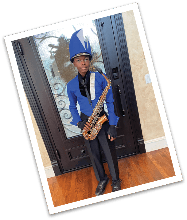 A person dressed in a blue and black marching band uniform with a tall blue hat is holding a saxophone while standing indoors in front of a glass door. Description generated by AI