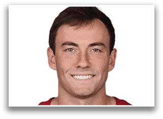A smiling adult with short dark hair and freckles is shown against a white background. Description generated by AI