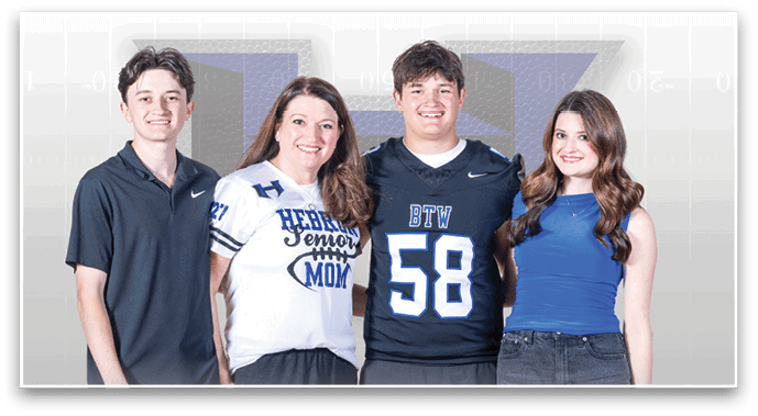 Four smiling people stand side by side against a light background, with one wearing a sports jersey, another wearing a shirt that says “Senior Mom," and the others dressed casually. Description generated by AI