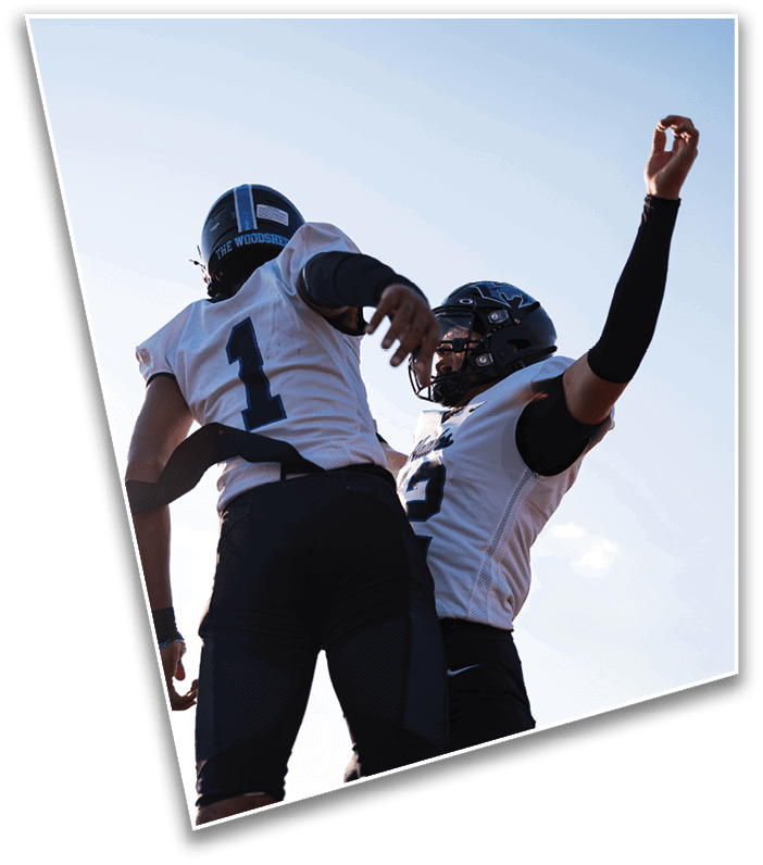 A person wearing a football helmet and gloves is holding up four fingers on one hand with a blurred football field and another player in the background. Description generated by AI