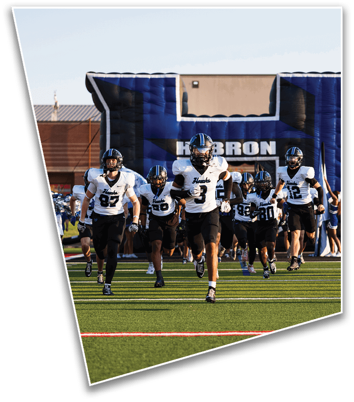 A person wearing a football helmet and gloves is holding up four fingers on one hand with a blurred football field and another player in the background. Description generated by AI