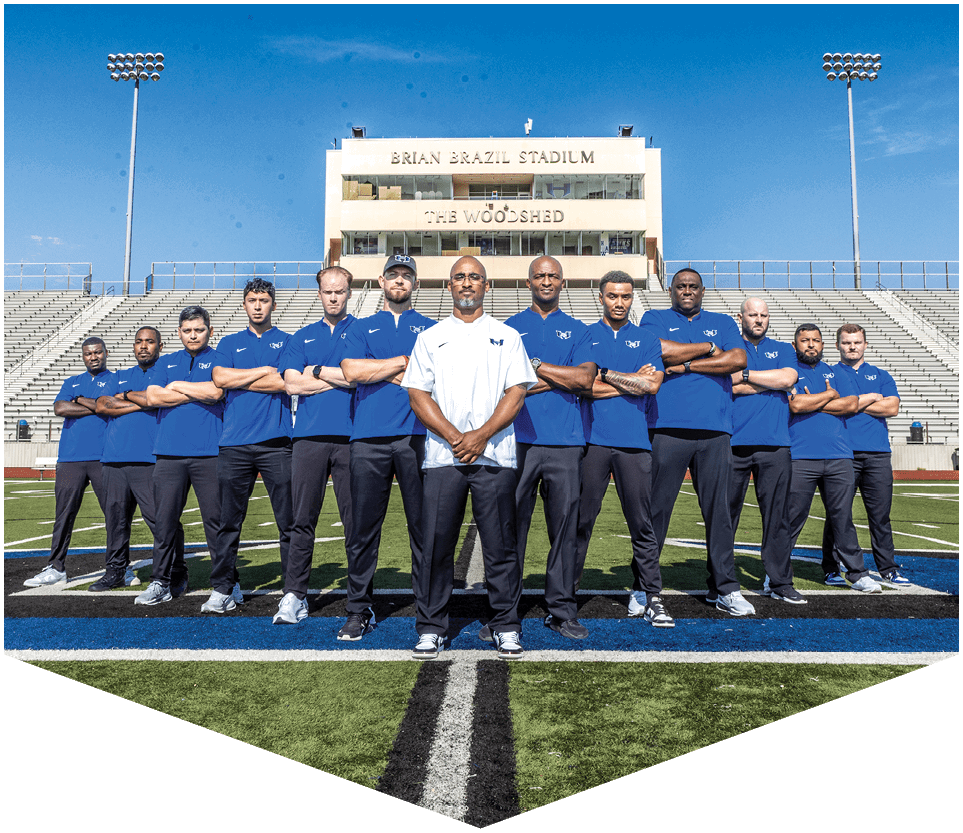 A group of nine people wearing black football uniforms with “HAWKS" written on the front stand side by side on a football field under a clear blue sky. Description generated by AI