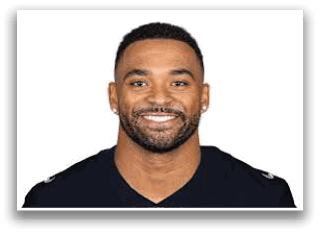 A person with short hair and a beard is smiling and wearing a dark shirt with a small emblem on the chest. Description generated by AI