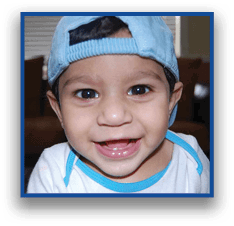 A child wearing a white shirt with blue trim is smiling and showing teeth. Description generated by AI
