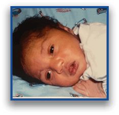A newborn wearing a white outfit lies on a blue blanket with colorful patterns and has a hospital wristband on one arm. Description generated by AI
