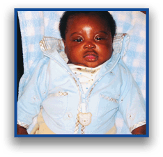 A child wearing a light blue jacket with a bear-shaped zipper pull is sitting against a blue and white checkered blanket. Description generated by AI