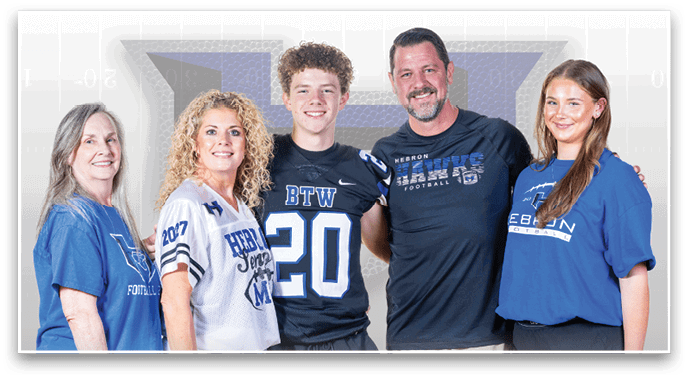 Five people wearing sports-themed shirts stand closely together smiling against a light background with a large faded letter. Description generated by AI