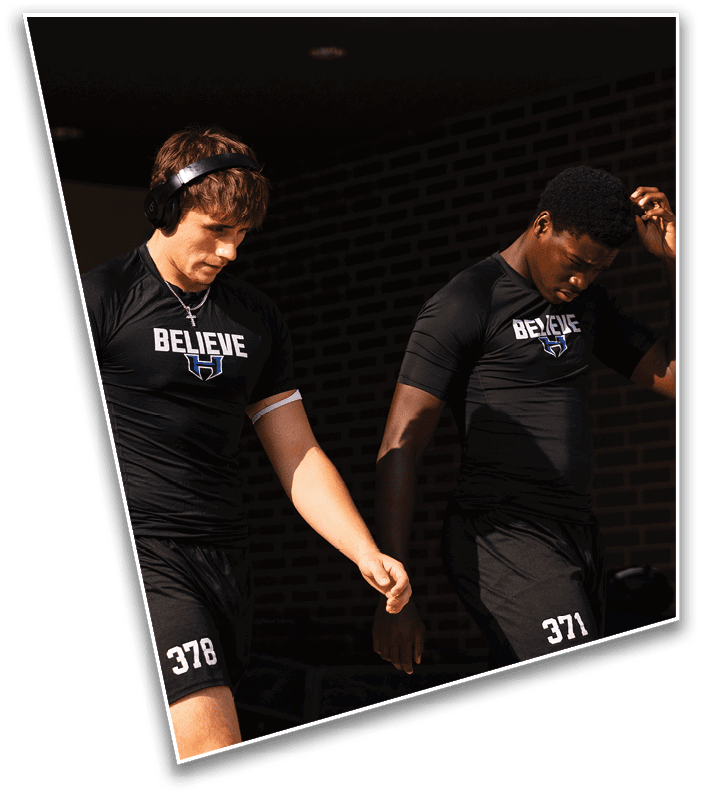 Two adults wearing black athletic clothing with the word “BELIEVE" printed on their shirts are walking side by side, one holding a phone and the other adjusting their hair. Description generated by AI