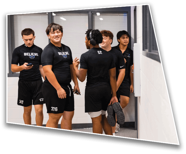 A group of people wearing black athletic clothing are standing and talking in a hallway with one person barefoot and another holding shoes. Description generated by AI