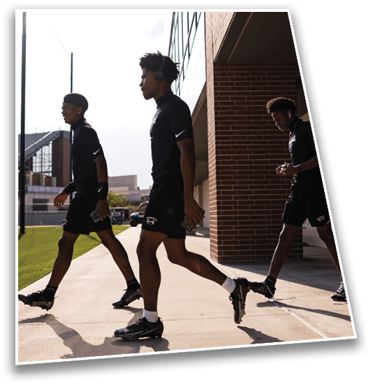Two people wearing black athletic clothing and headphones are walking outdoors near a sports stadium. Description generated by AI