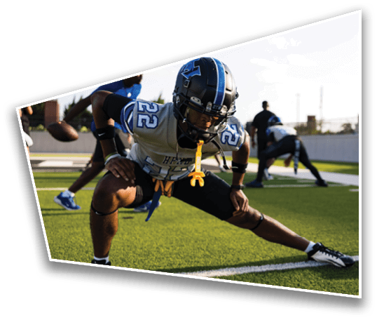A person wearing a football helmet and uniform is stretching on a field with other people in the background also preparing for practice. Description generated by AI