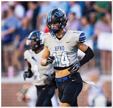 Two people in football uniforms and helmets are on a field with a blurred crowd in the background. Description generated by AI