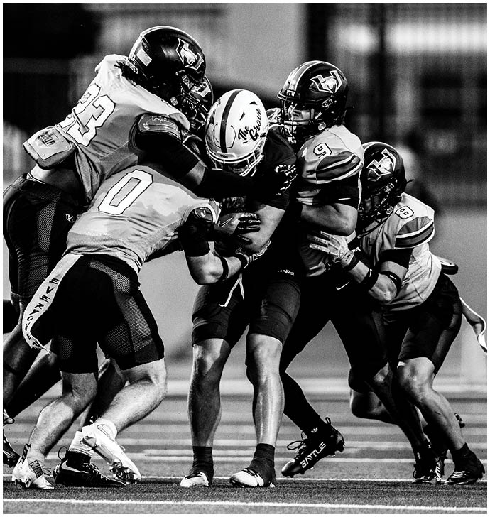 Four people in football uniforms are tackling a person in a different uniform who is holding a football on a field. Description generated by AI