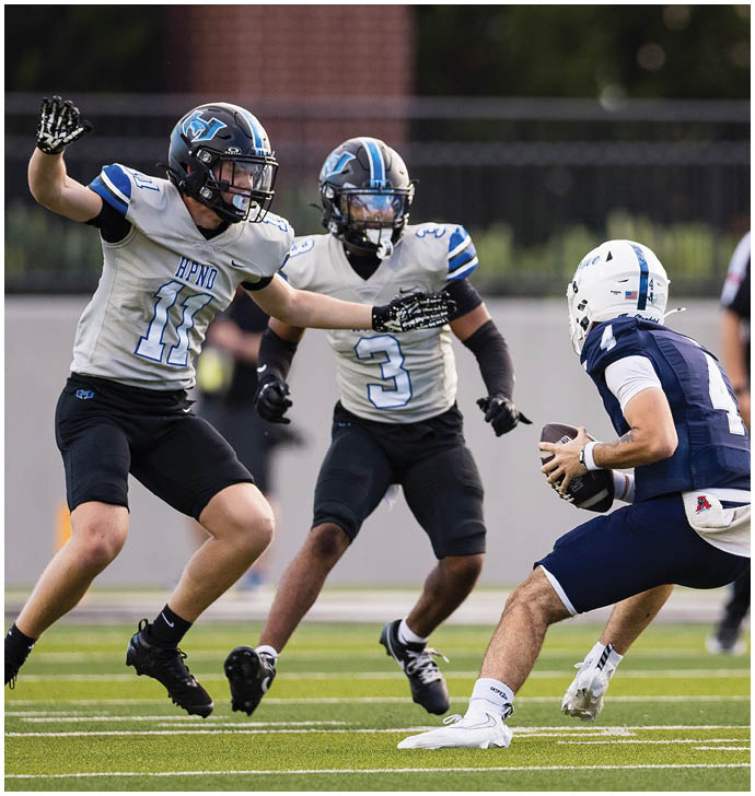 Three people in football uniforms are on a field with two players in light-colored jerseys moving toward a player in a dark-colored jersey holding a football. Description generated by AI