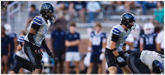 People in sports uniforms are positioned on a football field, preparing for a play during a game or practice. Description generated by AI