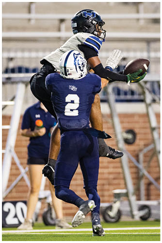 Two people in football uniforms are reaching for a football in mid-air during a game. Description generated by AI